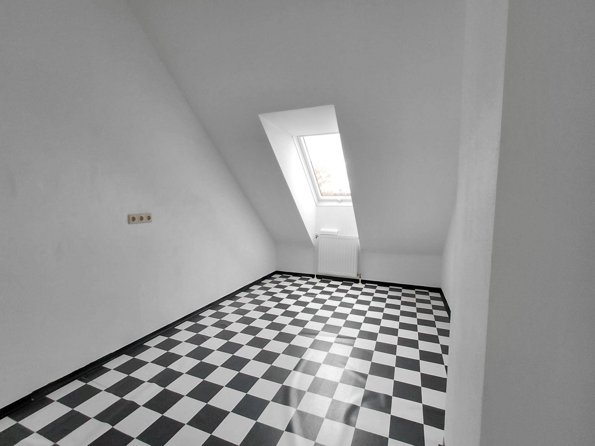 Helles Dachzimmer mit schwarz-weiß kariertem Boden, Dachfenster und Heizkörper.