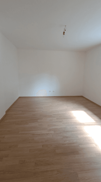 Helles, leeres Zimmer mit Laminatboden und weißen Wänden, bereit zur individuellen Gestaltung.