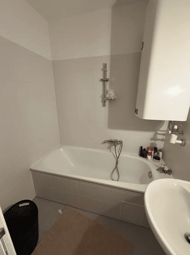 Helles Badezimmer mit Badewanne, Duschvorrichtung und Waschbecken, funktional ausgestattet.