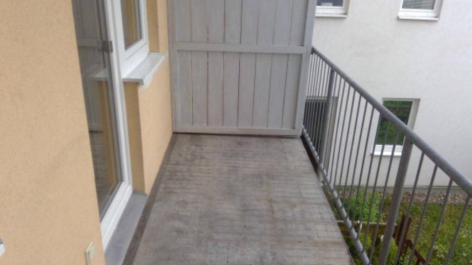 Schmaler Balkon mit Metallgeländer und Blick auf die umliegenden Gebäude und Grünflächen.