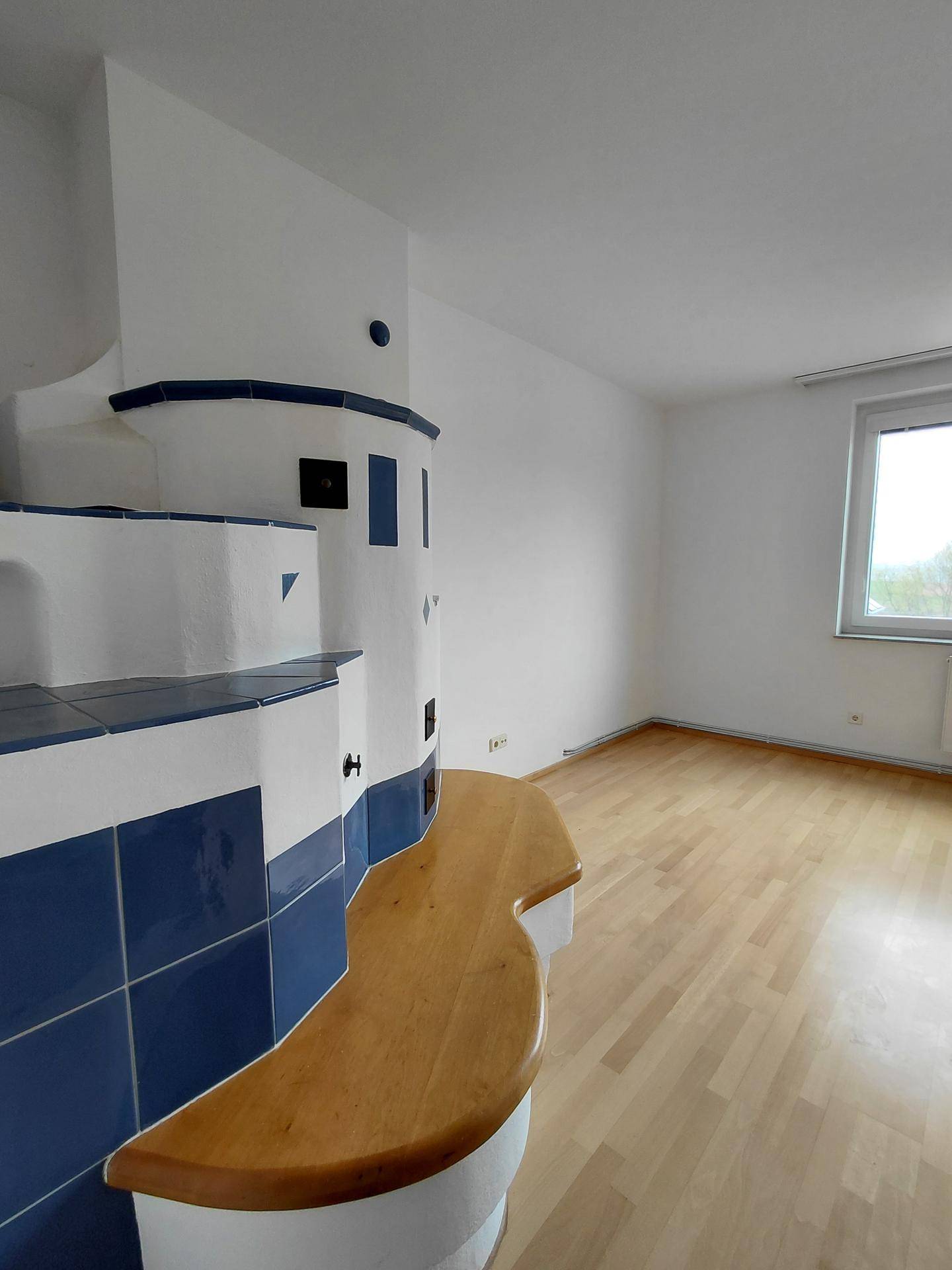 Heller Wohnraum mit Parkettboden und einem markanten blau-weißen Kachelofen als Blickfang.