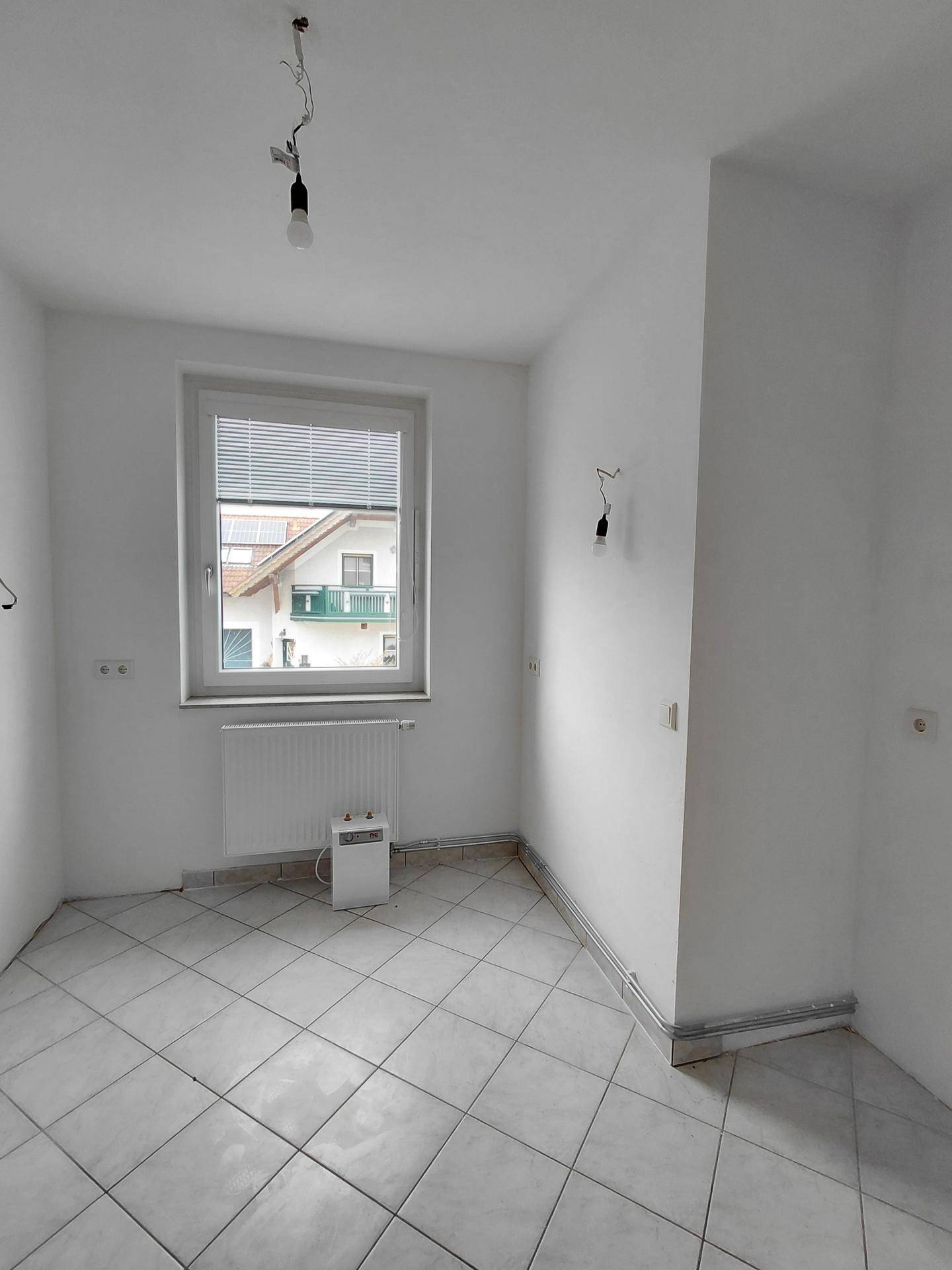 Leerer Raum mit hellen Fliesen, einem Fenster und einem Heizkörper, bereit zur Einrichtung.