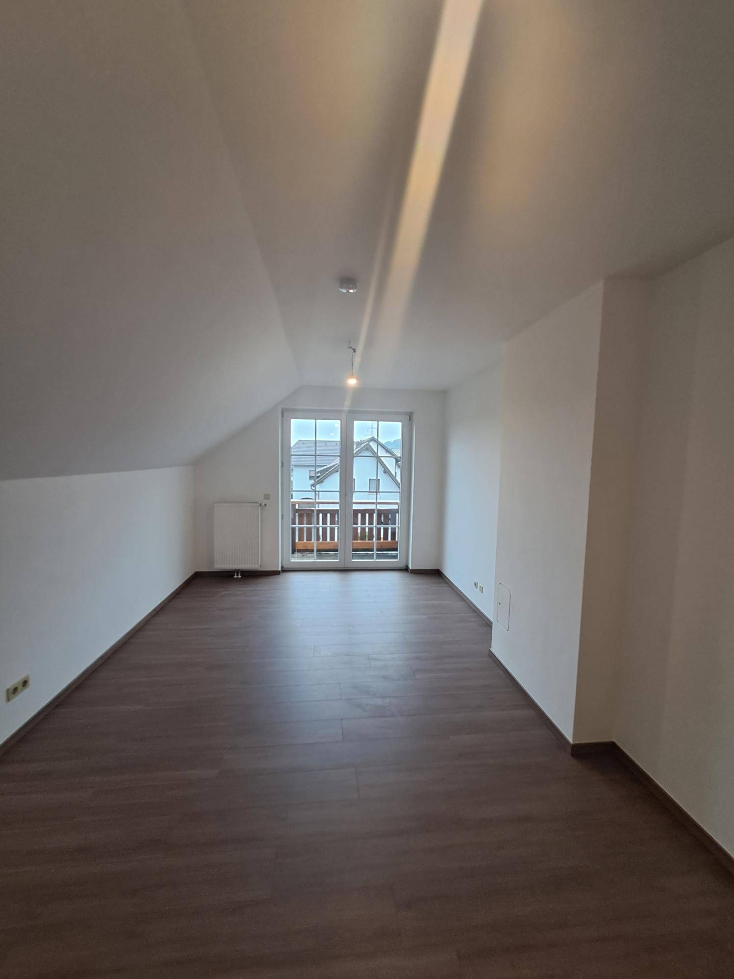 Geräumiges Zimmer im Dachgeschoss mit Laminatboden und Zugang zu einem kleinen Balkon.
