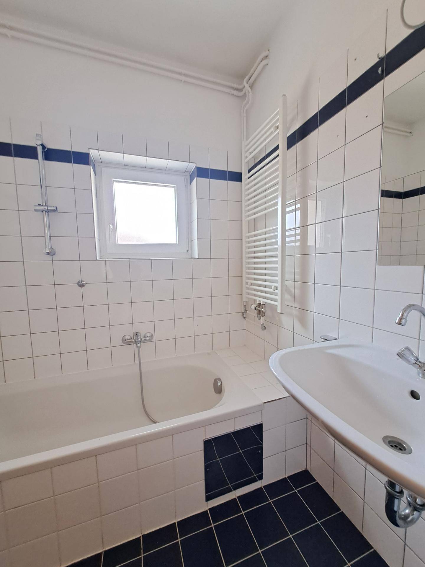 Gefliestes Badezimmer mit Badewanne, Waschbecken, Fenster und beheiztem Handtuchhalter.