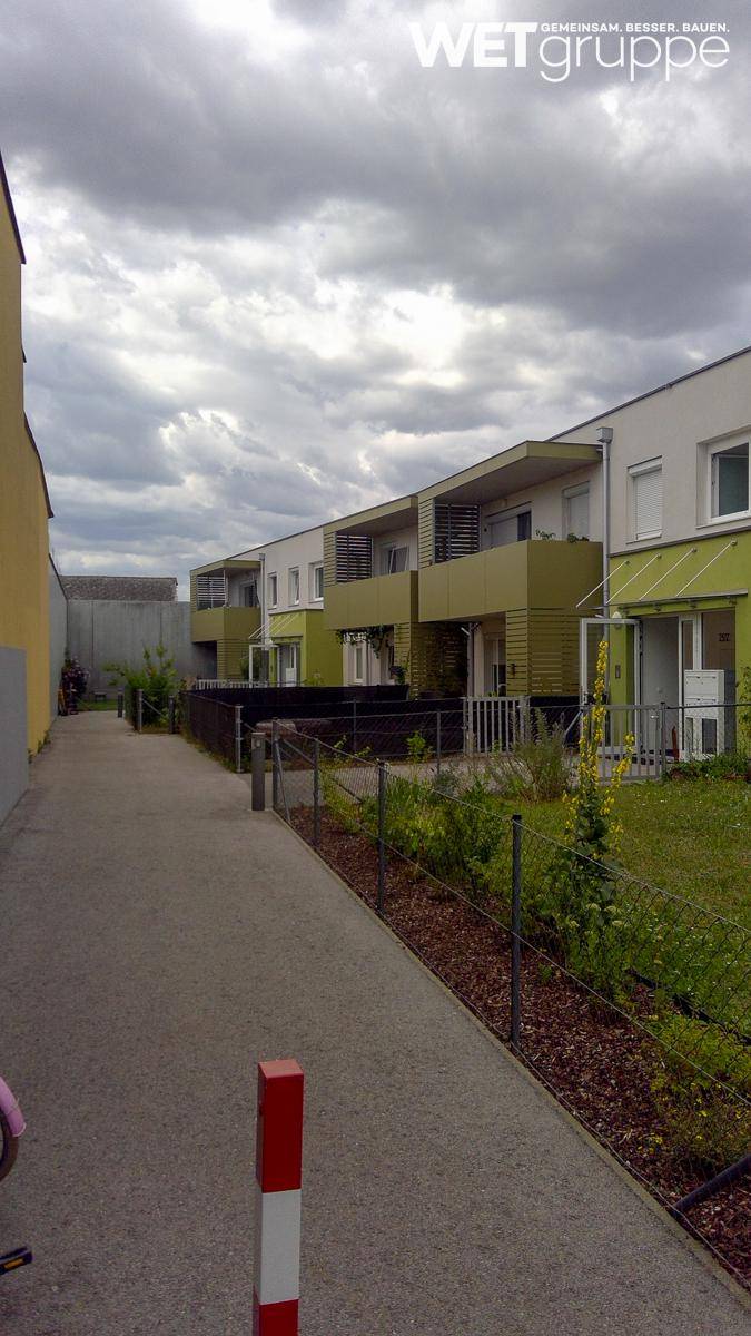 Moderne Reihenhäuser mit grünen Fassaden und Balkonen entlang eines Fußwegs.
