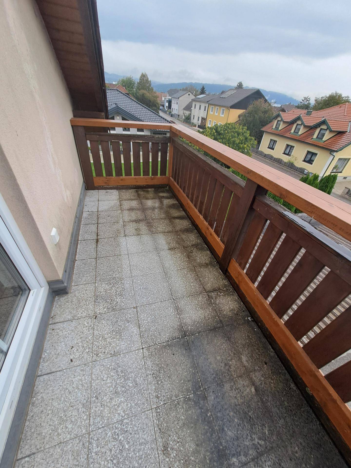 Kleiner Balkon mit Fliesenboden und Holzgeländer, bietet Blick auf die umliegende Wohngegend.