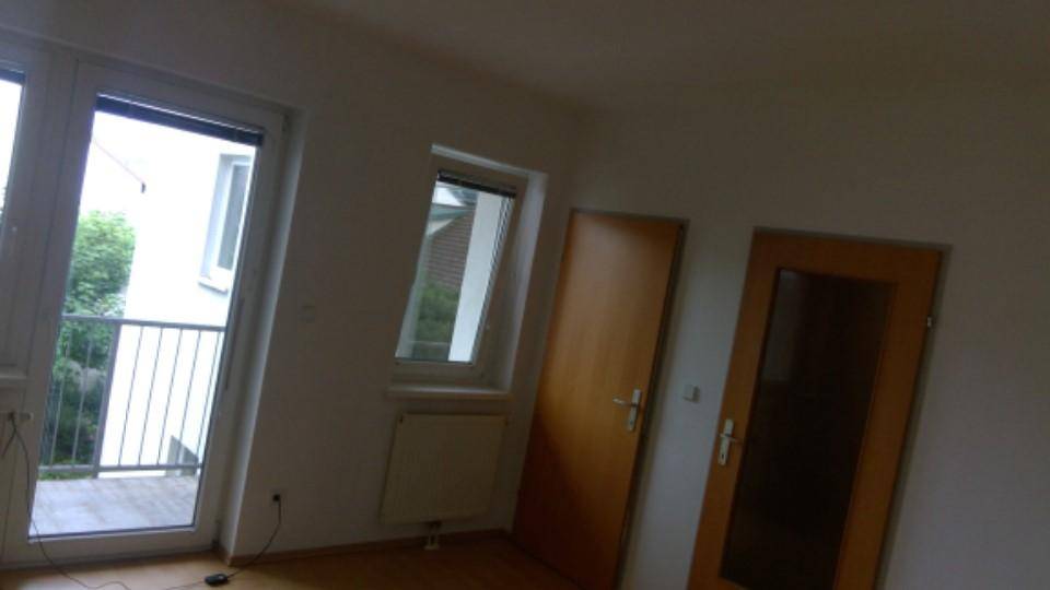Unmöblierter Raum mit Holzboden, Balkonzugang und zwei Holztüren, die zu weiteren Räumen führen.