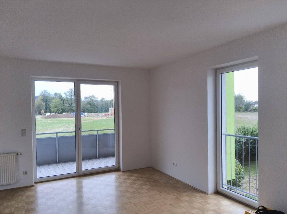 Geräumiger Raum mit Parkettboden, großen Fenstern und Zugang zu Balkonen mit weitem Grünblick.