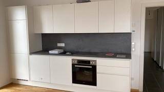 Moderne Einbauküche mit weißen Schränken, integriertem Backofen und dunkler Arbeitsplatte.