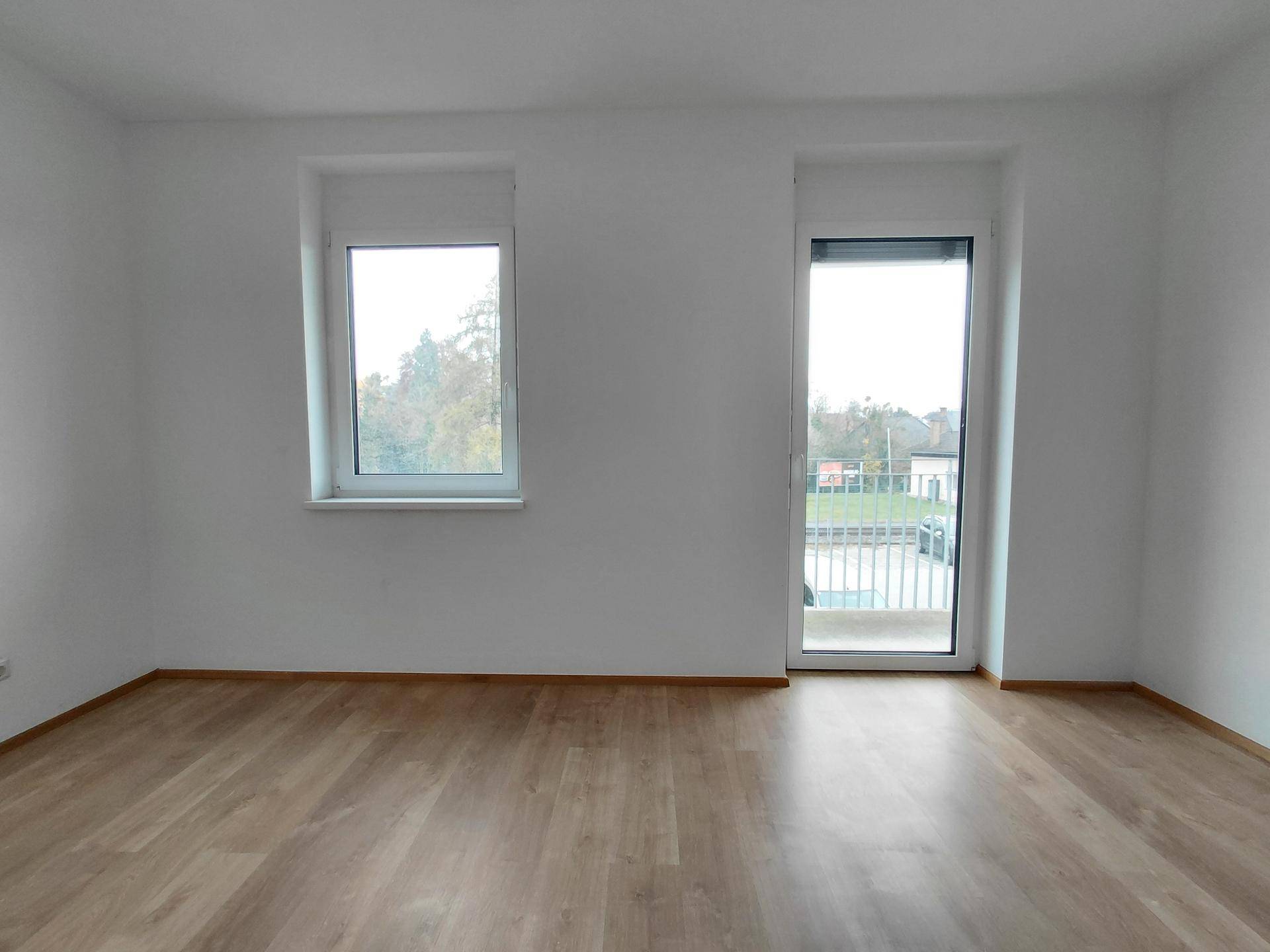 Geräumiges Zimmer mit Laminatboden und Fenstern mit Blick ins Freie.