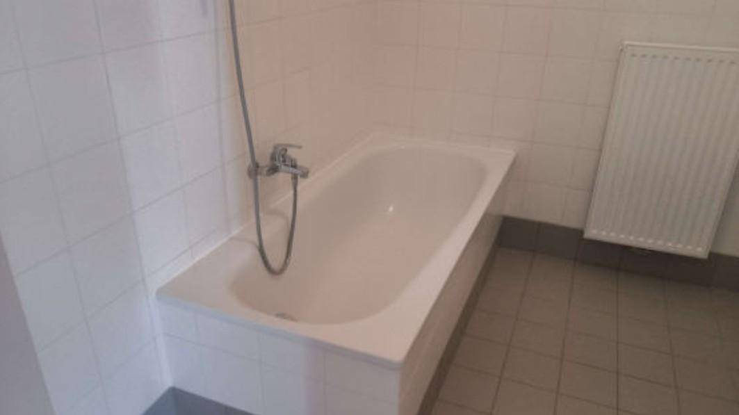 Einfaches Badezimmer mit weißer Badewanne und hellen Fliesen an Wänden und Boden.