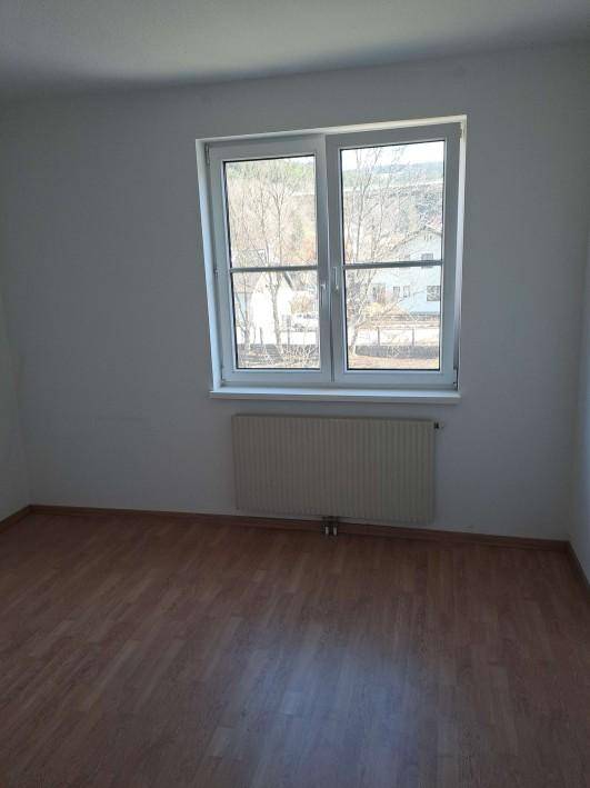 Freundliches Zimmer mit Holzboden, weiß gestrichenen Wänden und einem großen Fenster.