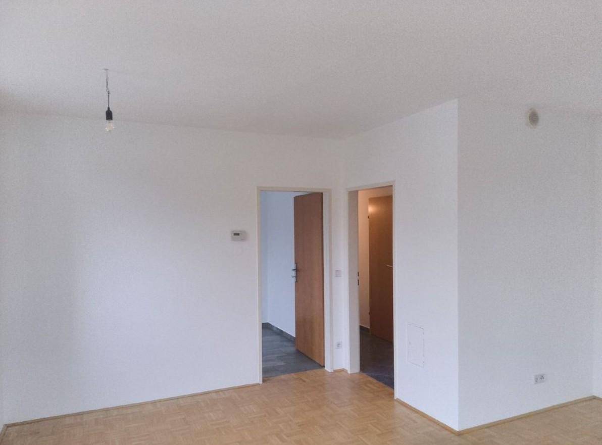 Heller, leerer Raum mit Parkettboden und zwei offenen Türen, die zu weiteren Zimmern führen.