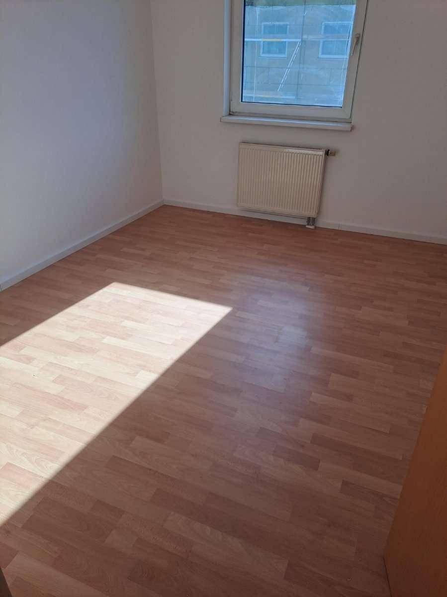 Leeres Zimmer mit Laminatboden, Heizkörper und Fenster mit Blick nach draußen.