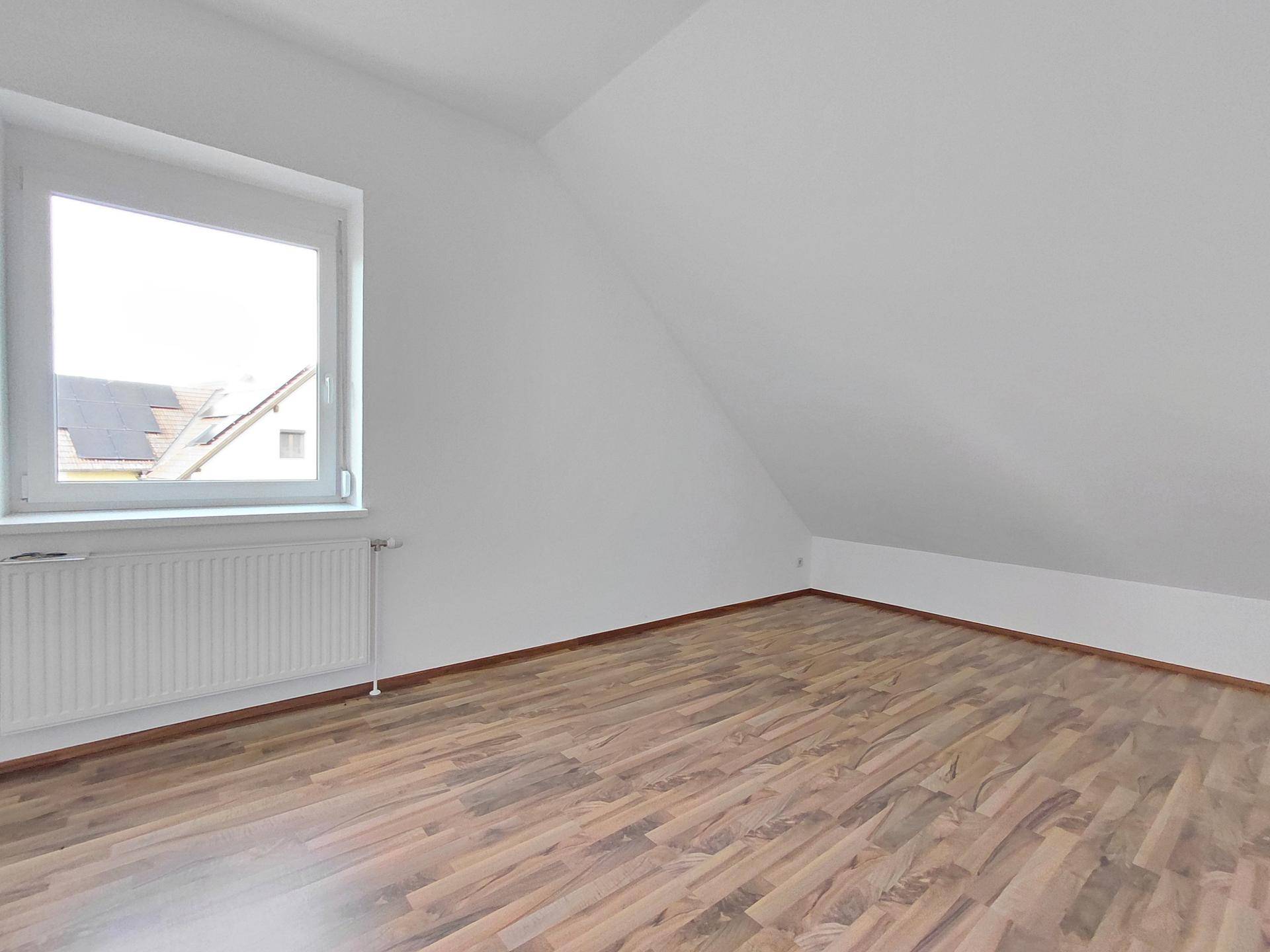 Helles Schlafzimmer im Dachgeschoss mit Schrägdecke, Fenster und Laminatboden.