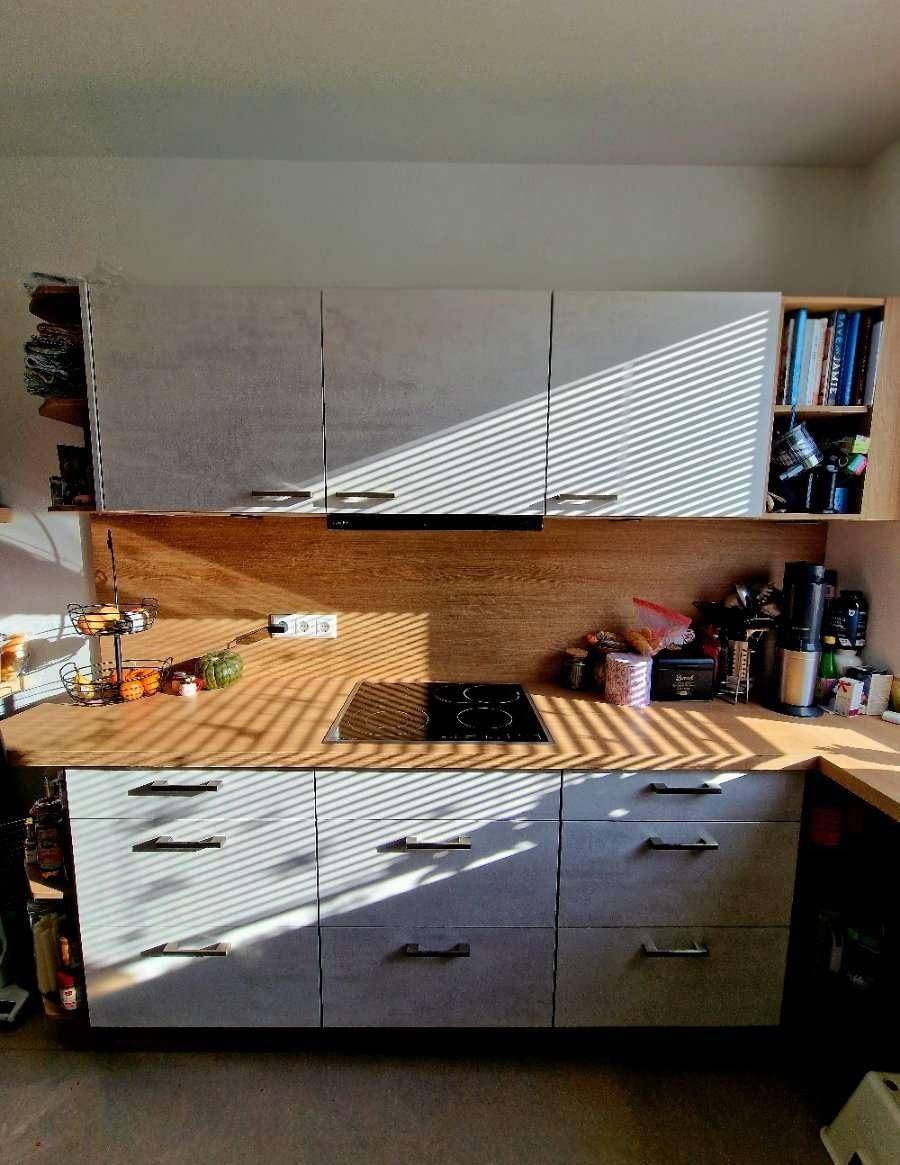Moderne Küche mit hellgrauen Schränken, Holzarbeitsplatte und Kochfeld.
