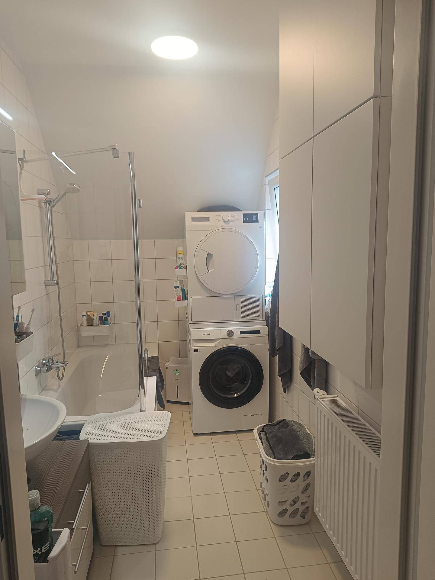 Modernes Badezimmer mit Badewanne, Dusche, Waschmaschine und Trockner sowie weißen Fliesen.