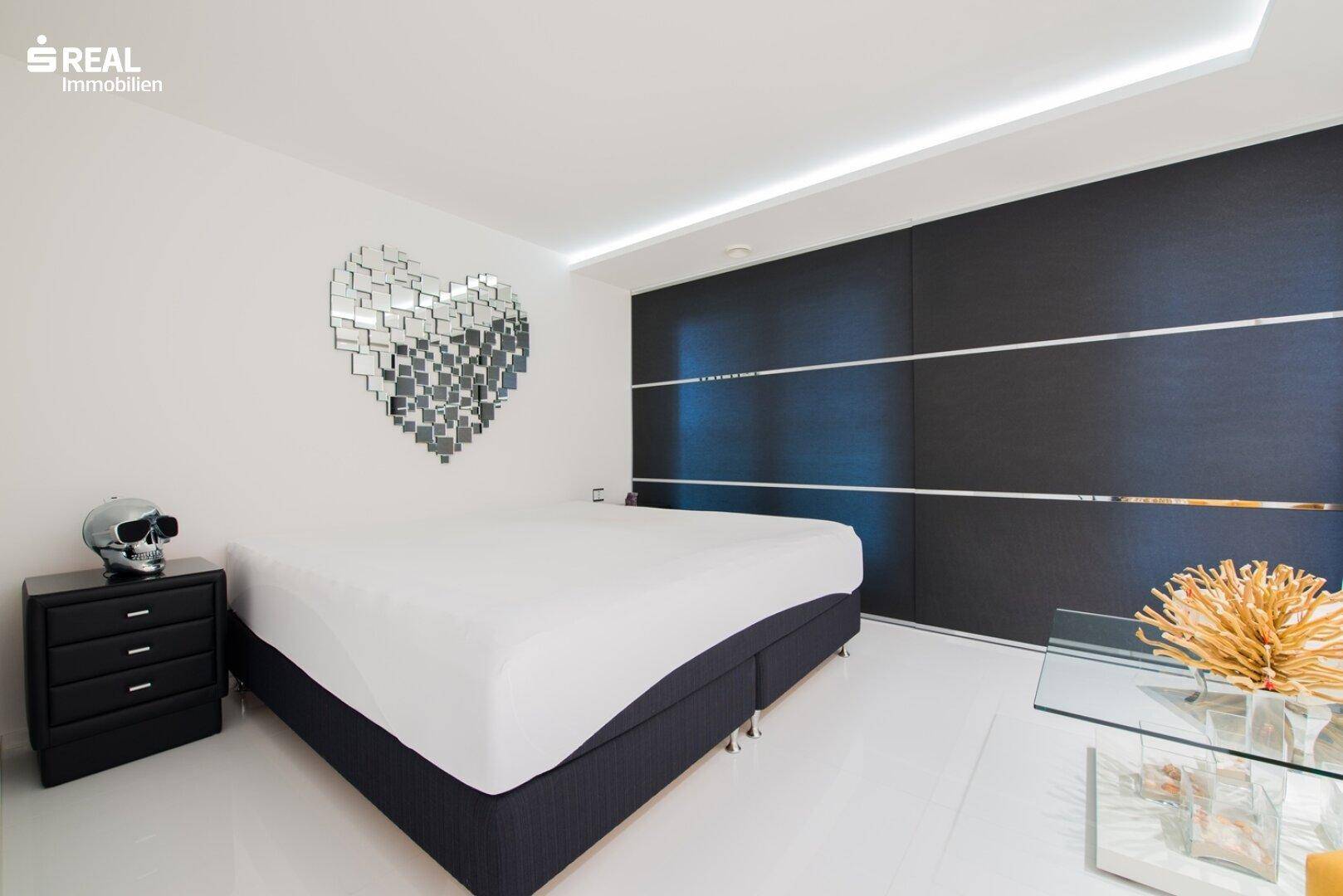 Schlafzimmer mit großem Bett, dunklen Schiebetüren und einem auffälligen Spiegel in Herzform.