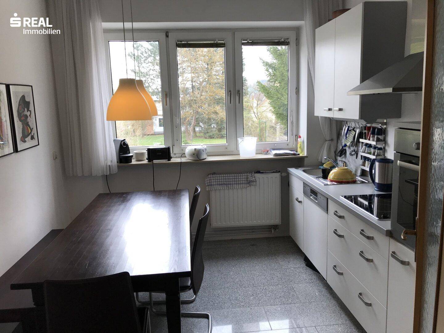 Helle Wohnküche mit weißer Einbauküche, Esstisch und Blick ins Grüne.