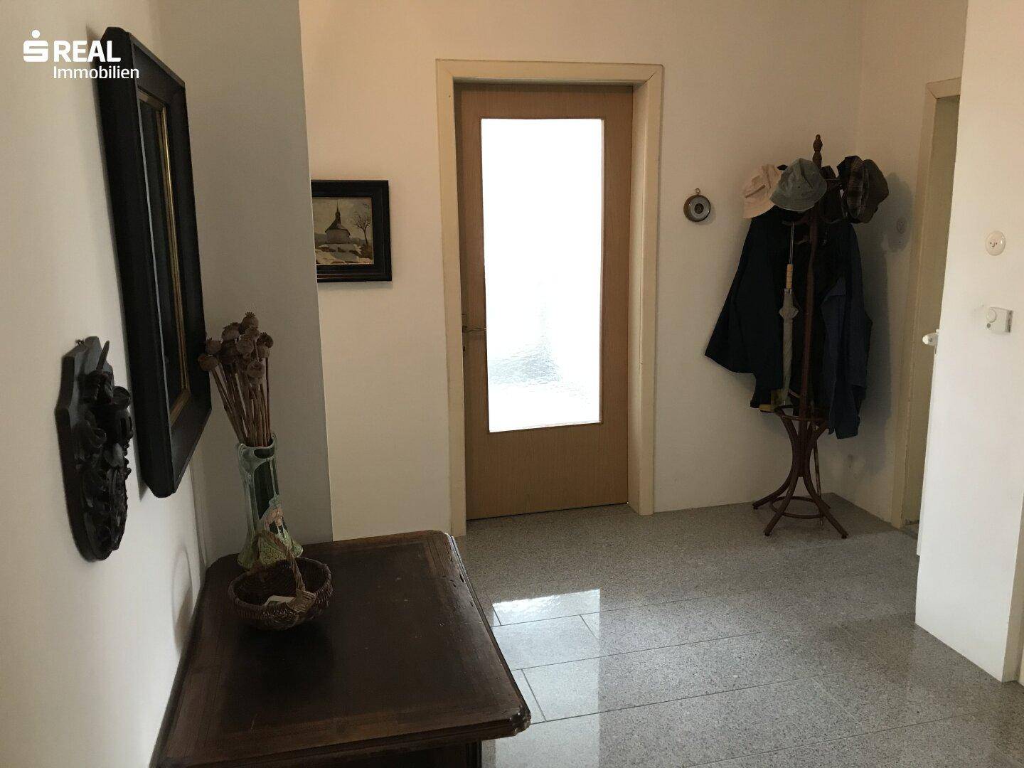 Heller Flur mit glänzenden Fliesen, Garderobe und Holztür.