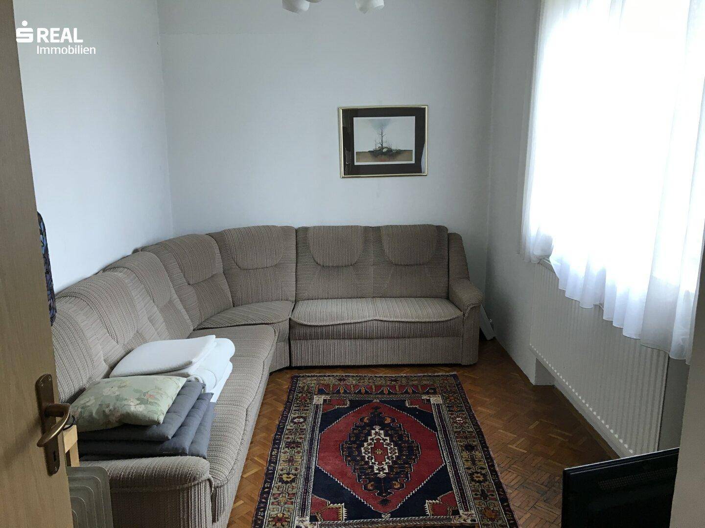Gemütliches Wohnzimmer mit Ecksofa, Teppich und Parkettboden.