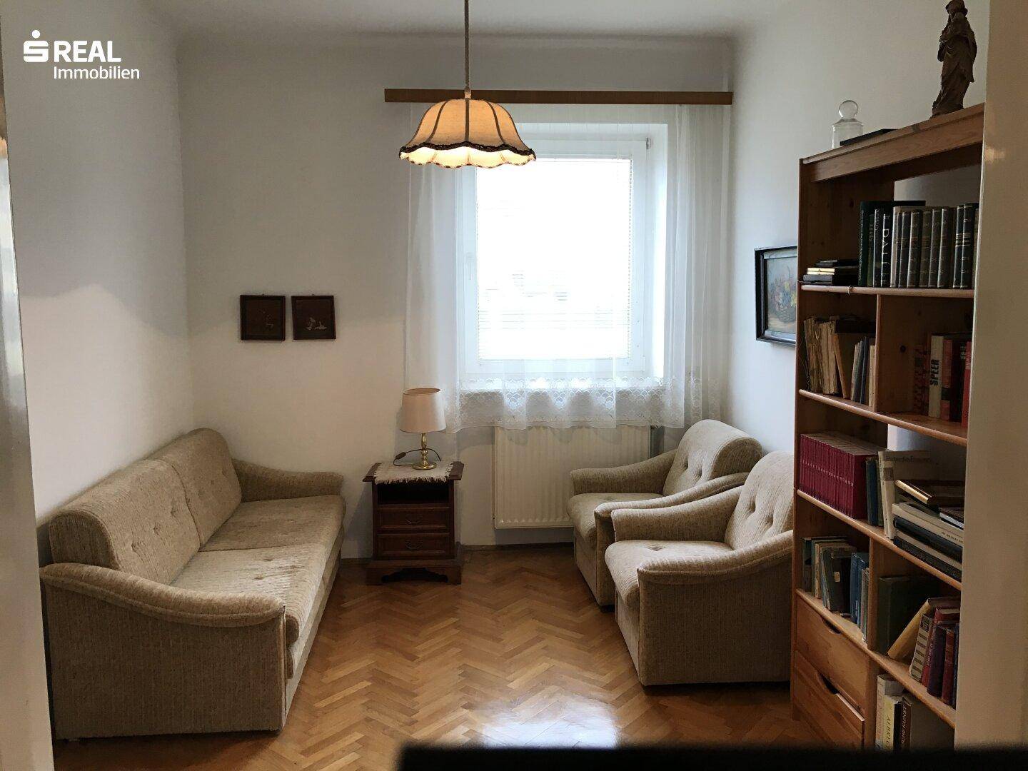 Gemütliches Wohnzimmer oder Arbeitszimmer mit Sofa, Bücherregal und Parkettboden.