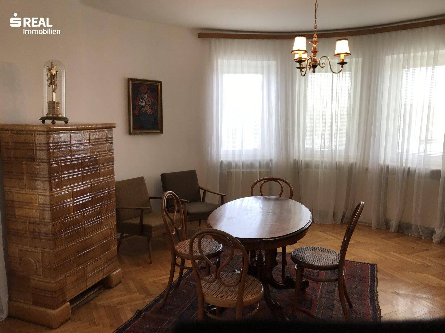 Wohnzimmer mit traditionellem Kachelofen, Holztisch und Parkettboden.