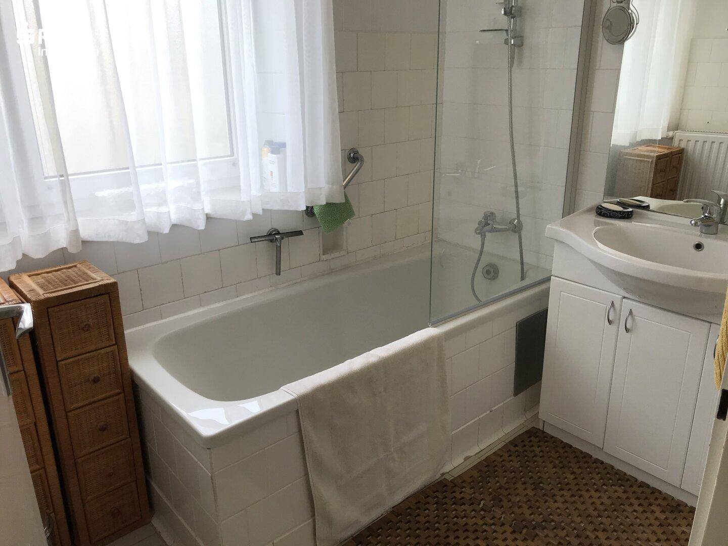 Badezimmer mit Badewanne, Duschabtrennung und Fenster.
