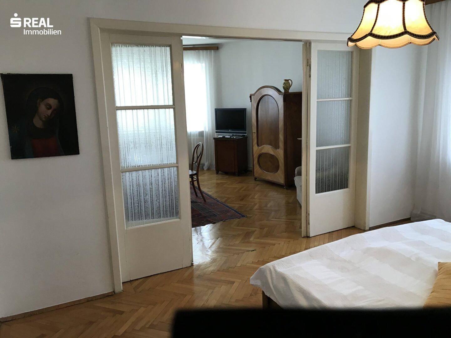 Schlafzimmer mit Parkettboden und Schiebetüren, die zu einem weiteren Raum führen.