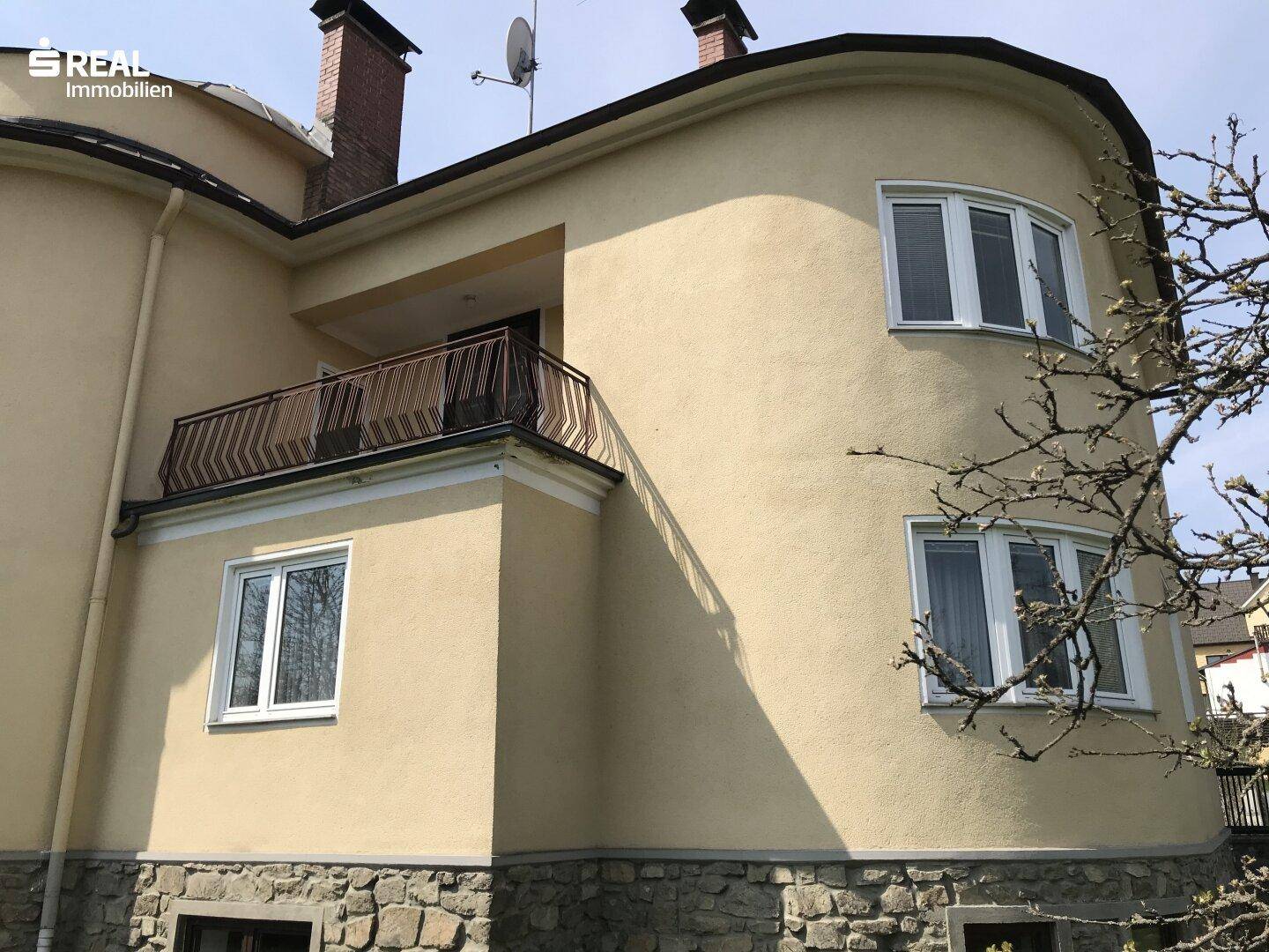 Seitenansicht des Hauses mit gelber Fassade, runden Fenstern und einem Balkon.