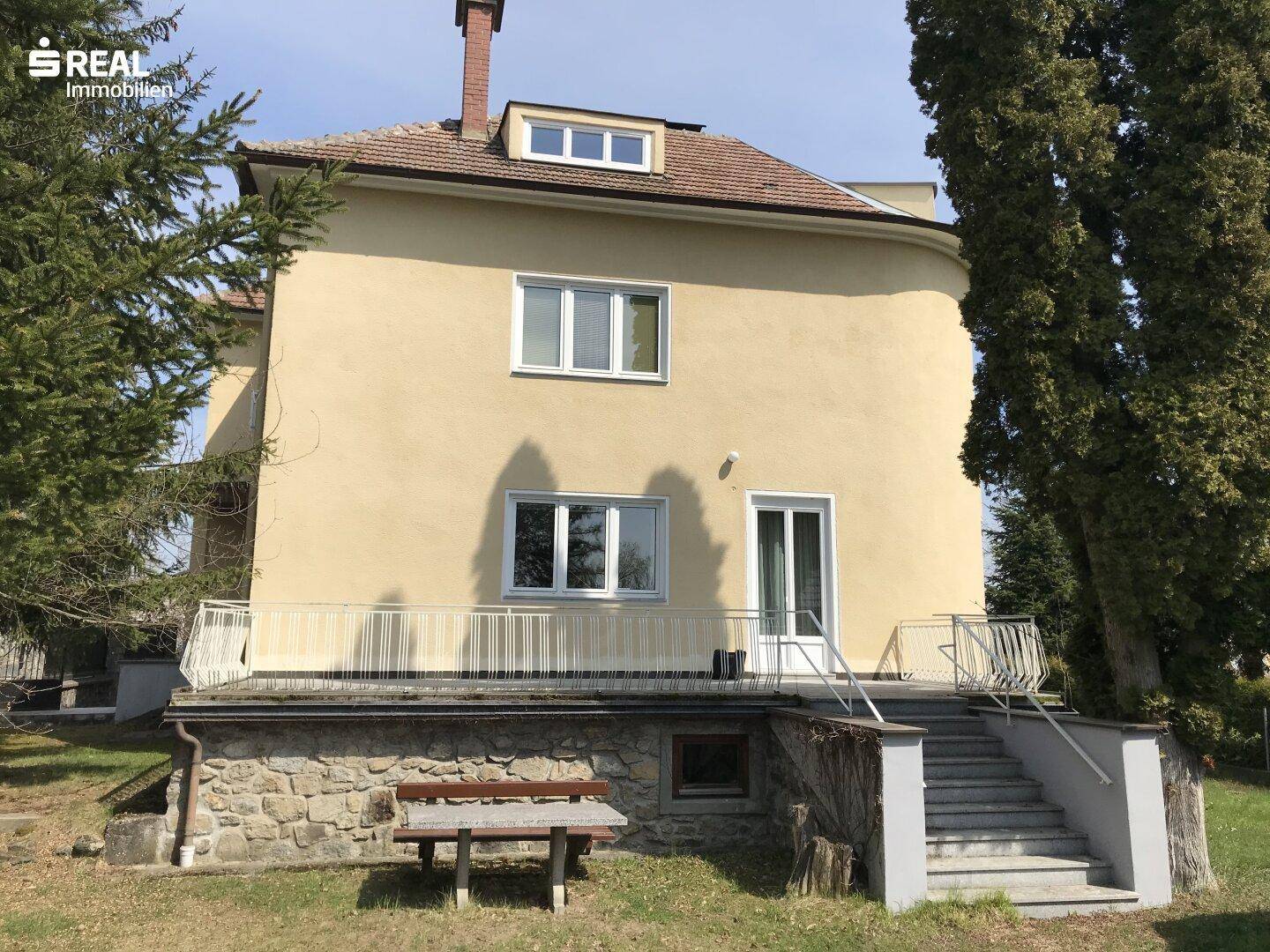 Rückseite des Hauses mit einer Terrasse im Erdgeschoss und Zugang zum Garten über eine Treppe.