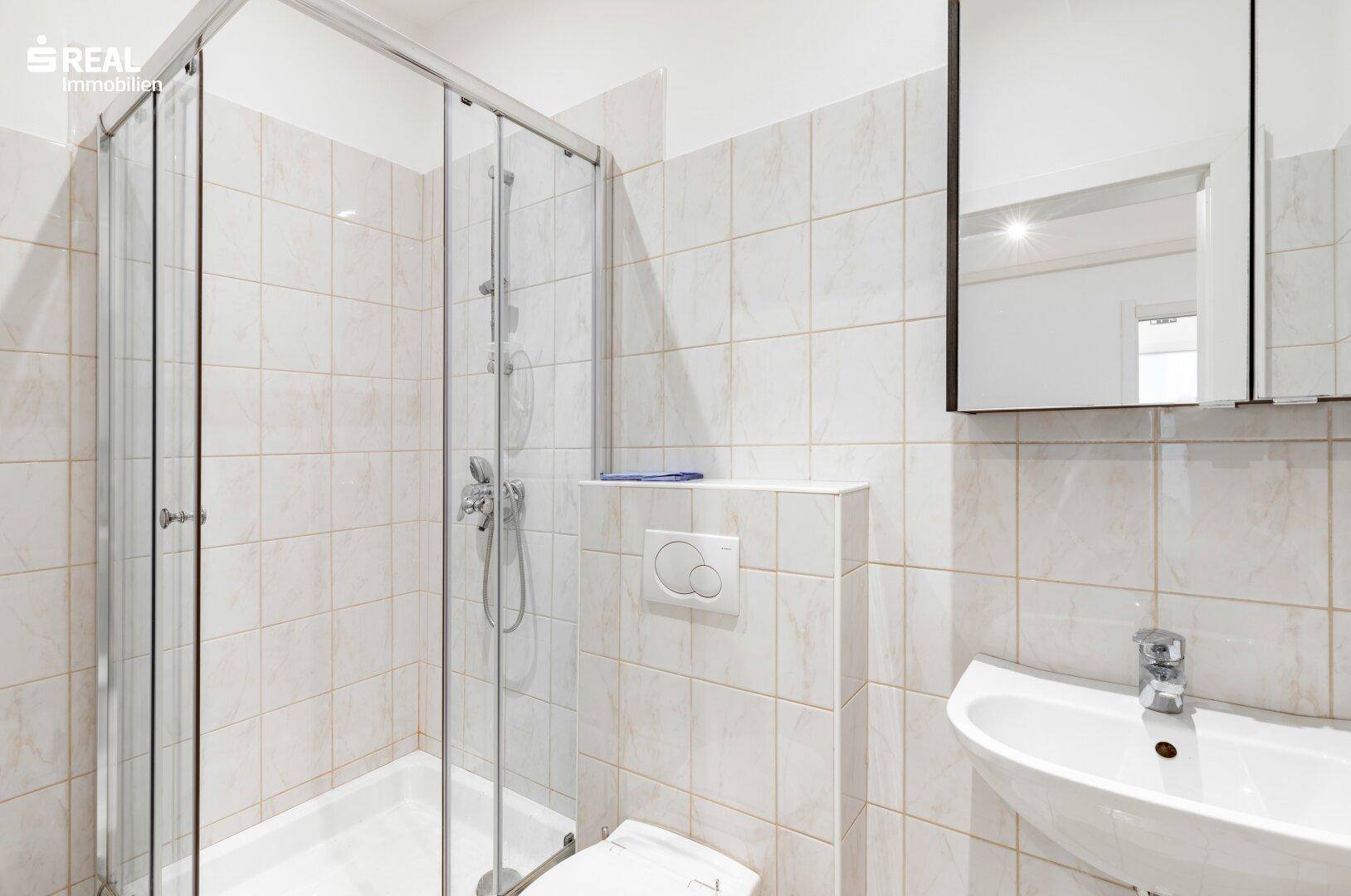 Funktionales Badezimmer mit Duschkabine, WC, Waschbecken und Spiegelschrank.