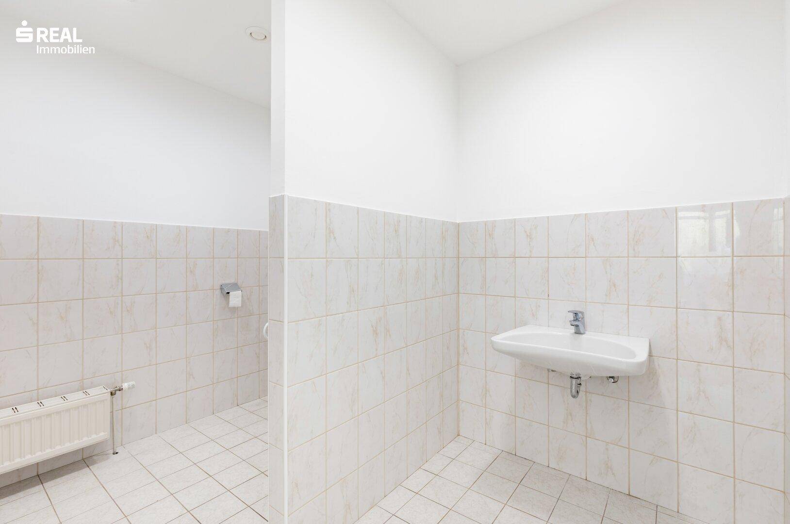 Badezimmer mit weißen Fliesen, einem Waschbecken und einem Heizkörper.