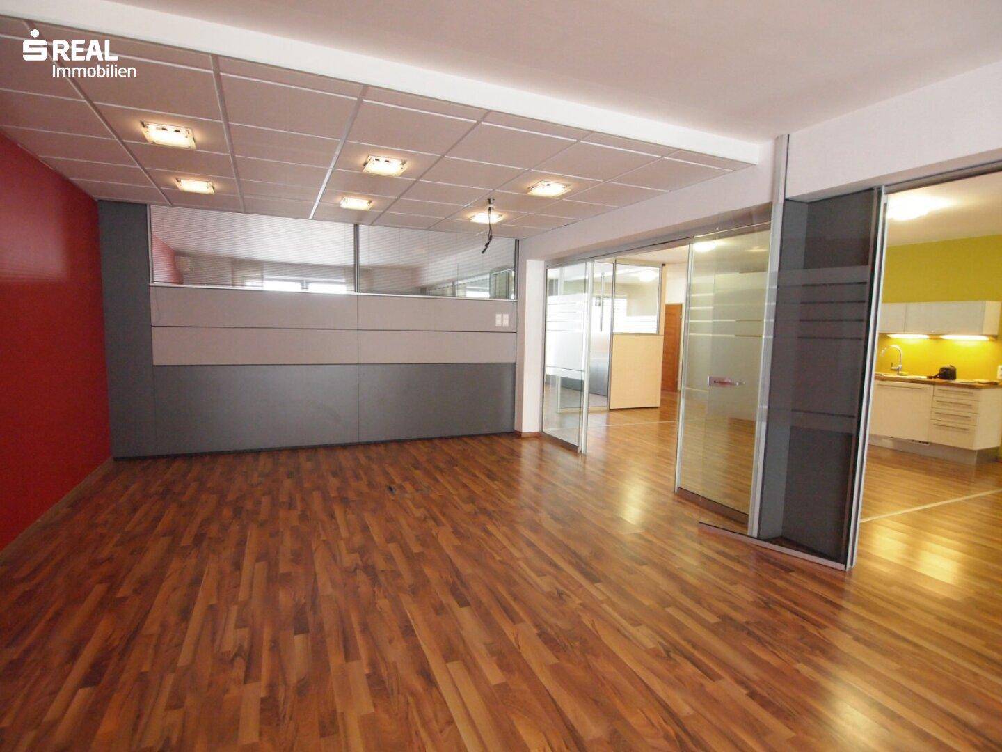 Großzügiger Büroraum mit Holzboden, abgehängter Decke und modernen Trennwänden, die separate Arbeitsbereiche schaffen.