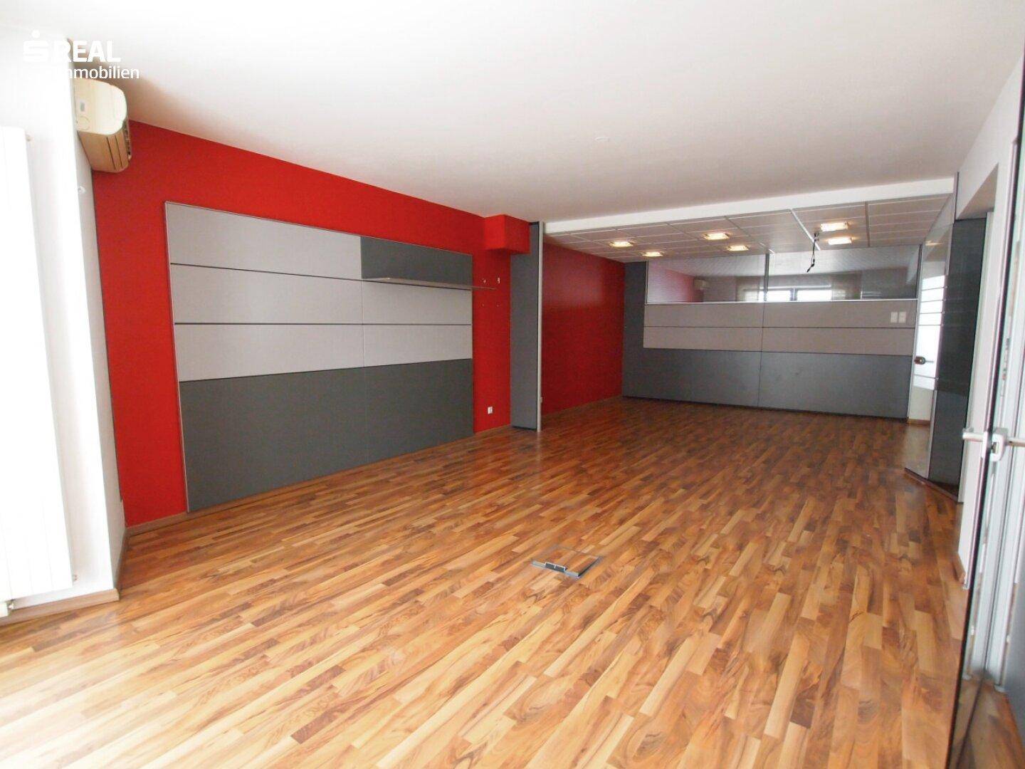 Langer Bürobereich mit roter Akzentwand, Holzboden und modularen Trennwänden, die den Raum strukturieren.