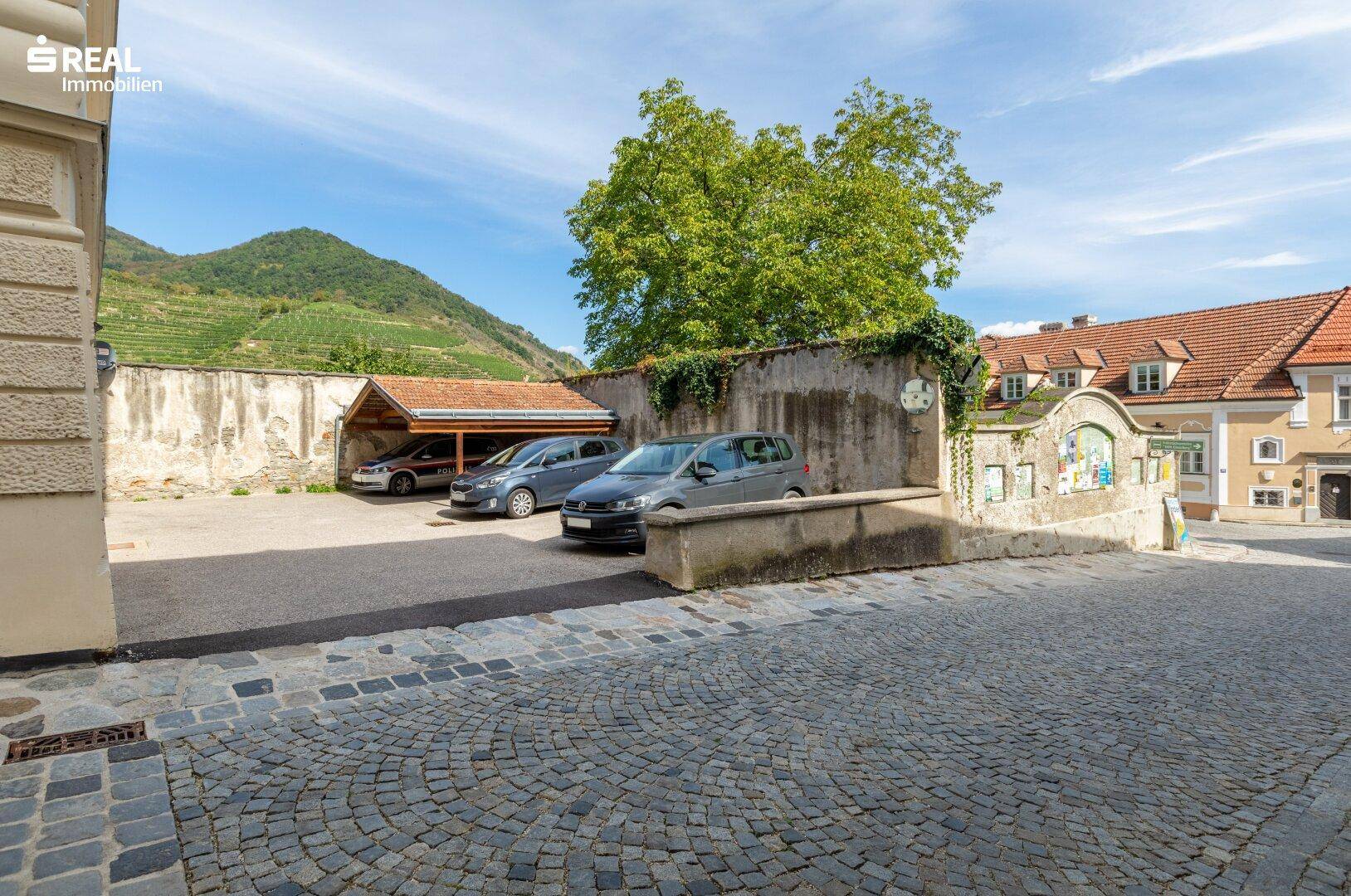 Parkplatz mit überdachten Stellplätzen und Blick auf die umliegenden Weinberge und Berge.