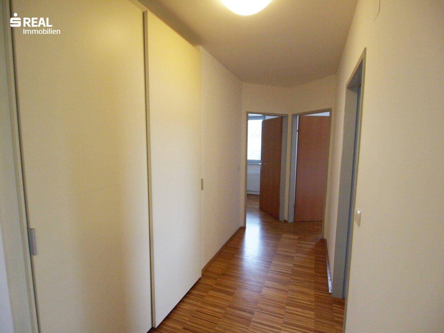Langer Flur mit Holzboden und weißen Einbauschränken, der Zugang zu mehreren Zimmern bietet.
