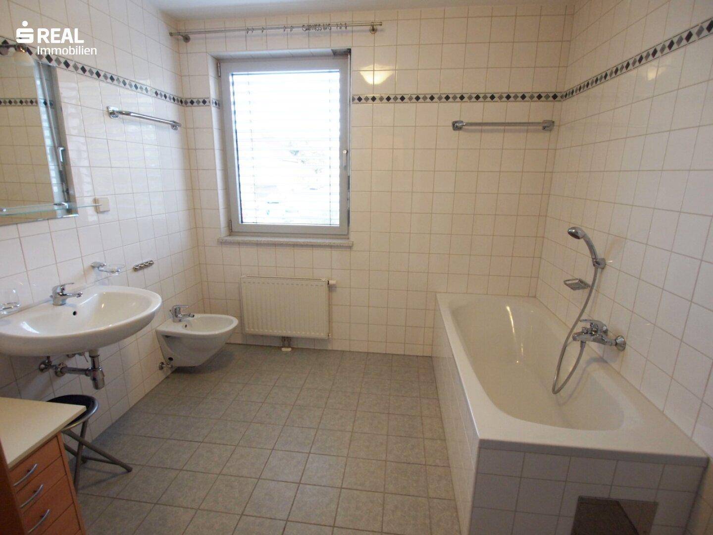 Gefliestes Badezimmer mit Badewanne, Waschbecken, Bidet und einem Fenster für Tageslicht.