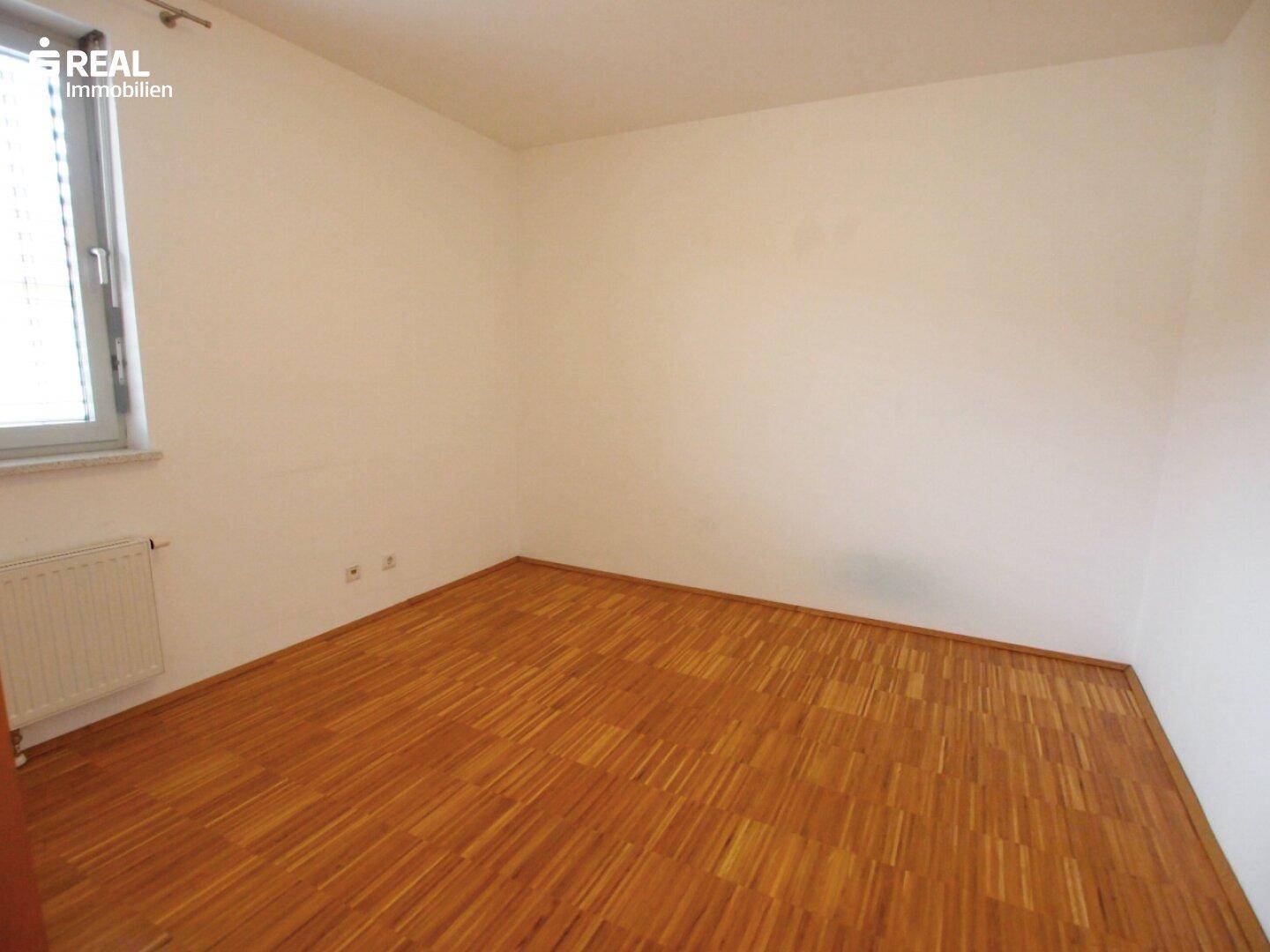 Helles Schlafzimmer mit Parkettboden und einem Fenster, das für natürliche Belichtung sorgt.