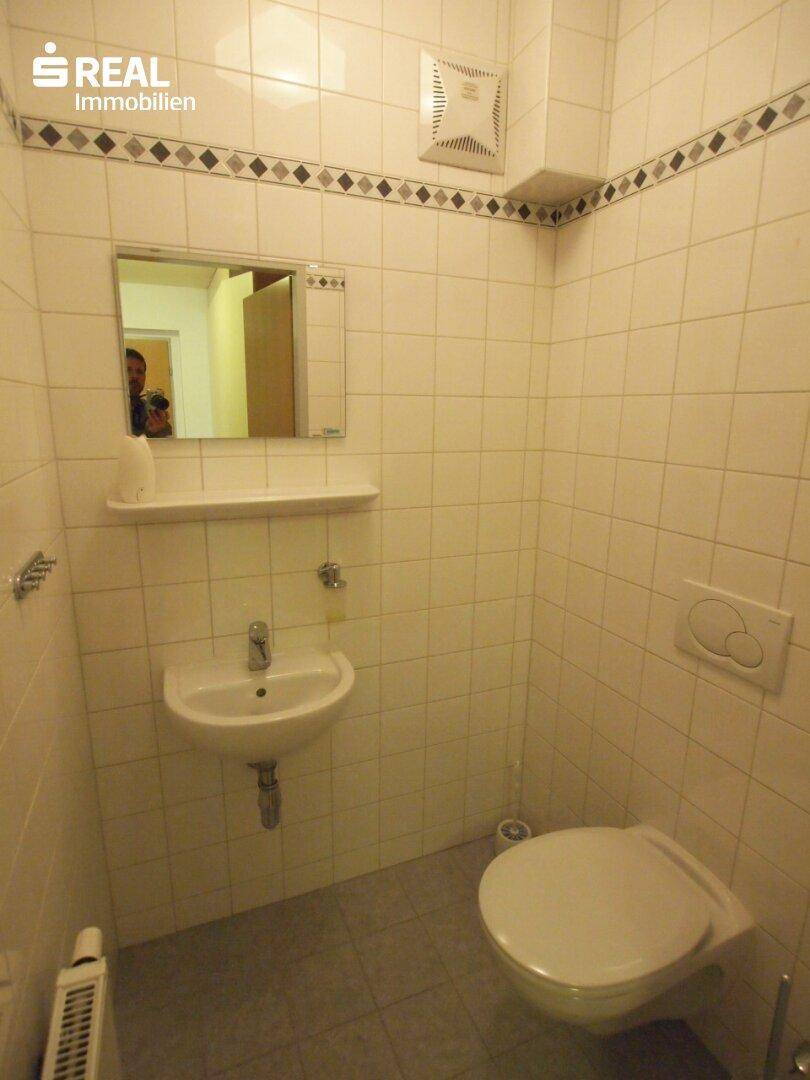 Kleines Gäste-WC mit Wand-WC, Waschbecken und Fliesen an Wänden und Boden.