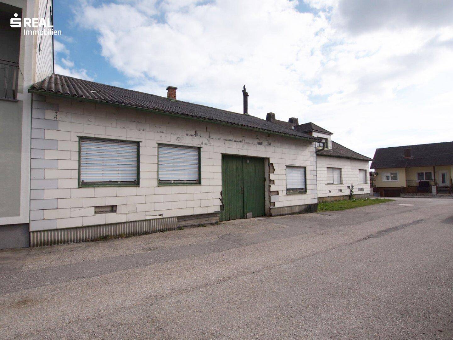 Ansicht der Gebäudefassade mit grünen Garagentoren und Fenstern mit Rollläden.