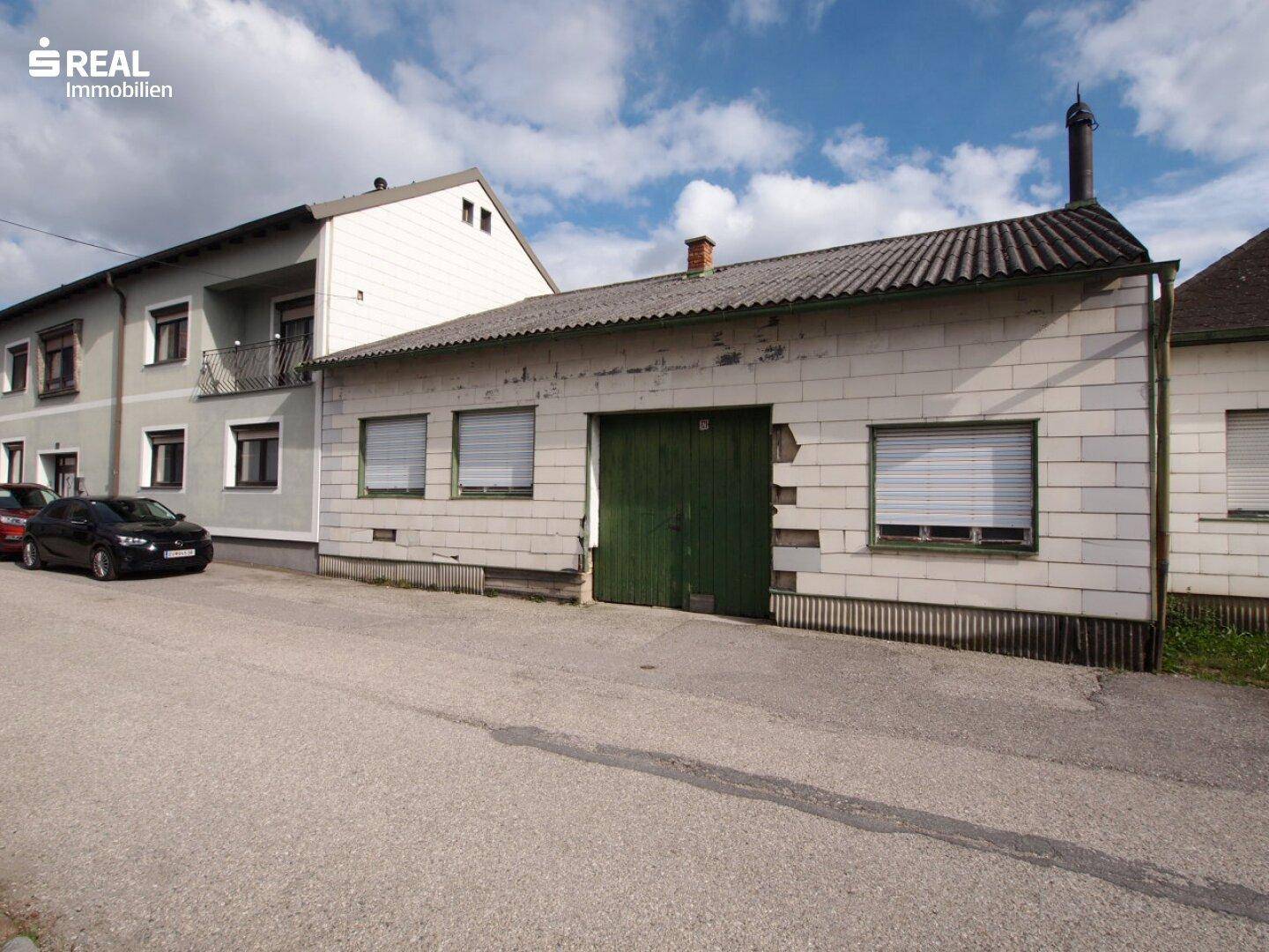 Gebäudeansicht mit grünen Garagentoren, Rollläden und einem angrenzenden Wohnhaus.