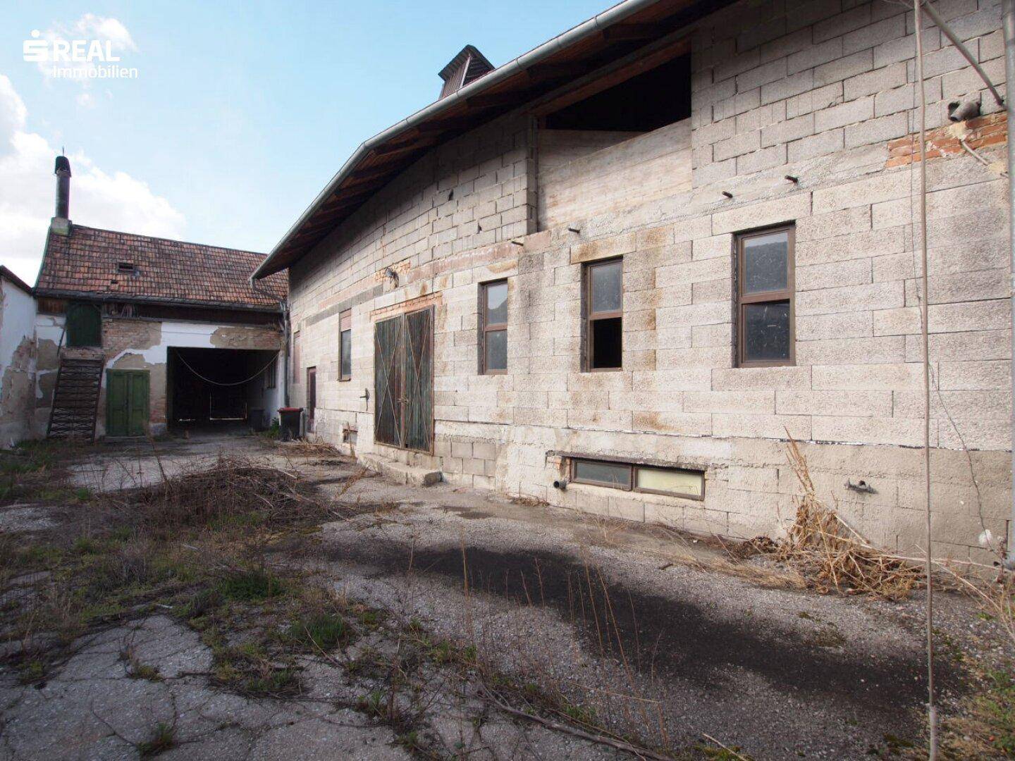 Altes Nebengebäude aus Betonsteinen mit ungepflegtem Hofbereich und Holztüren.