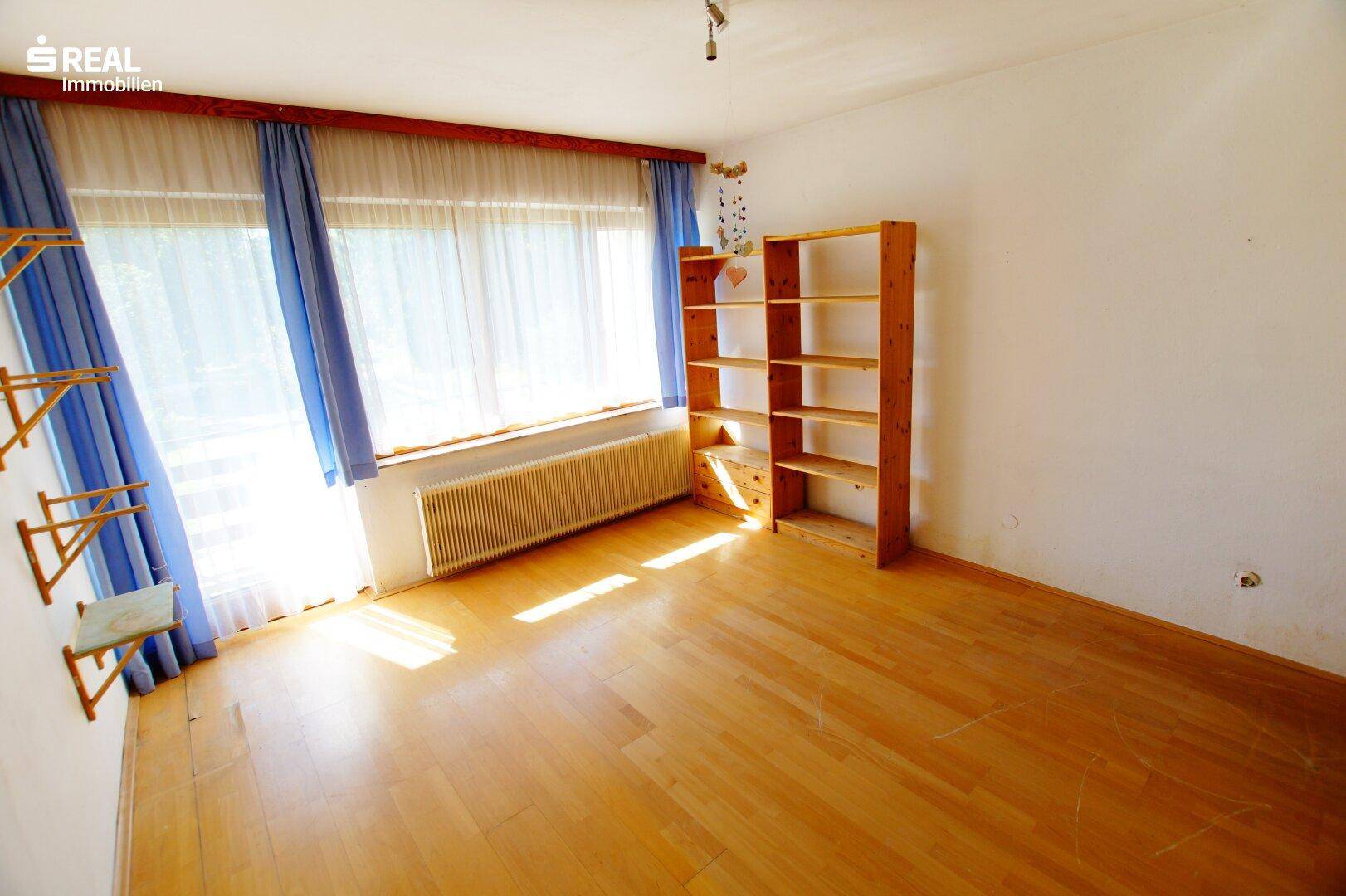 Heller Raum mit Parkettboden, blauen Vorhängen und einem Holzregal, ideal als Wohn- oder Schlafzimmer.