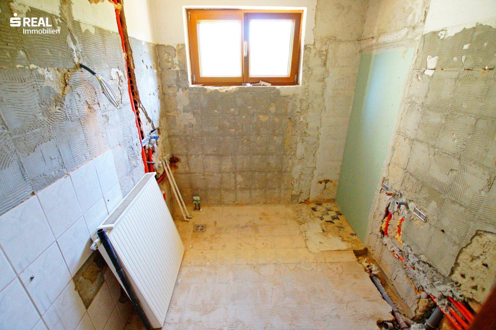 Badezimmer im Rohzustand mit freiliegenden Wänden und Leitungen, bereit für die Renovierung.