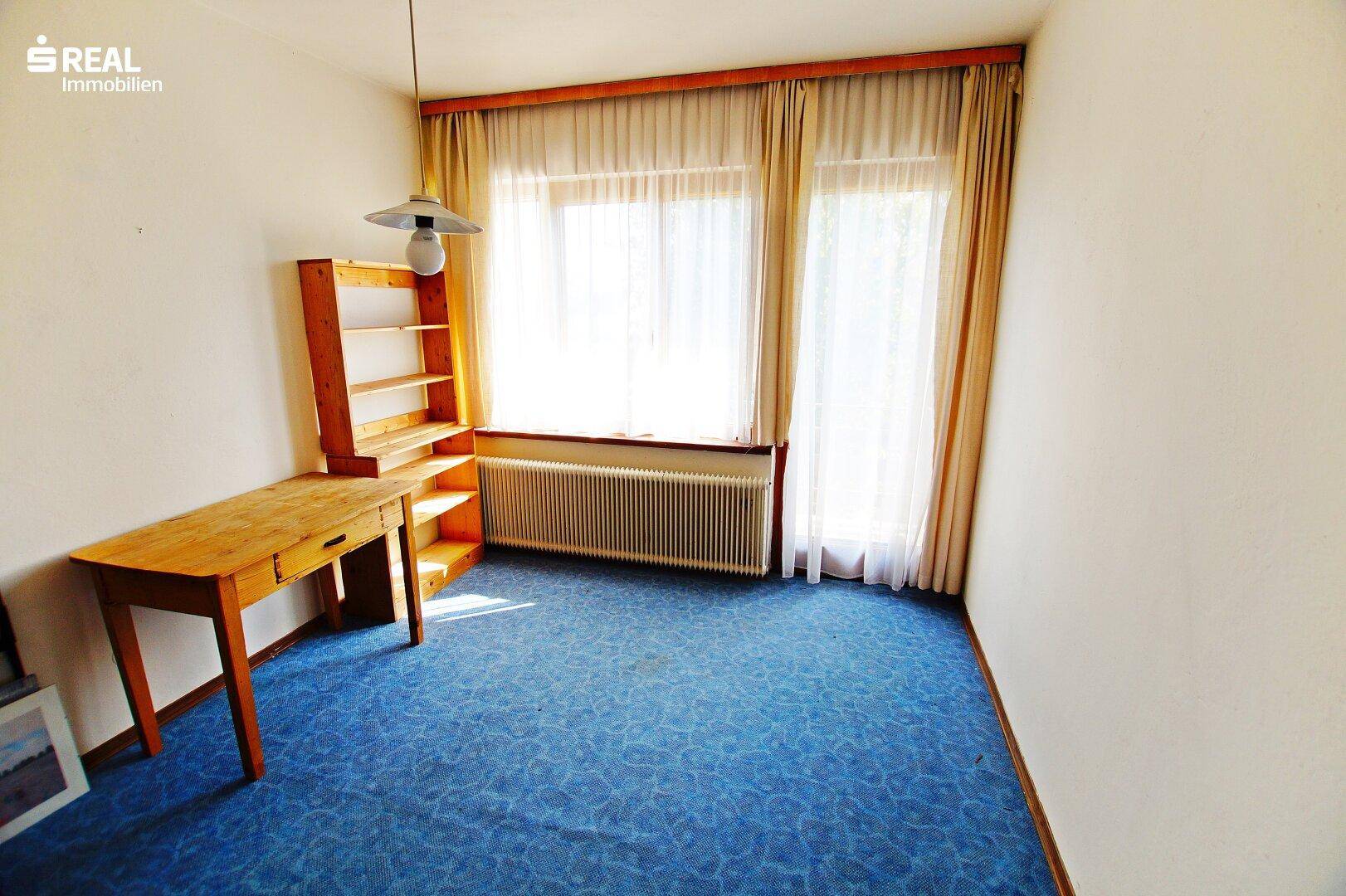 Arbeitszimmer mit blauem Teppichboden, Holzschreibtisch und Regal, ideal für Home-Office.