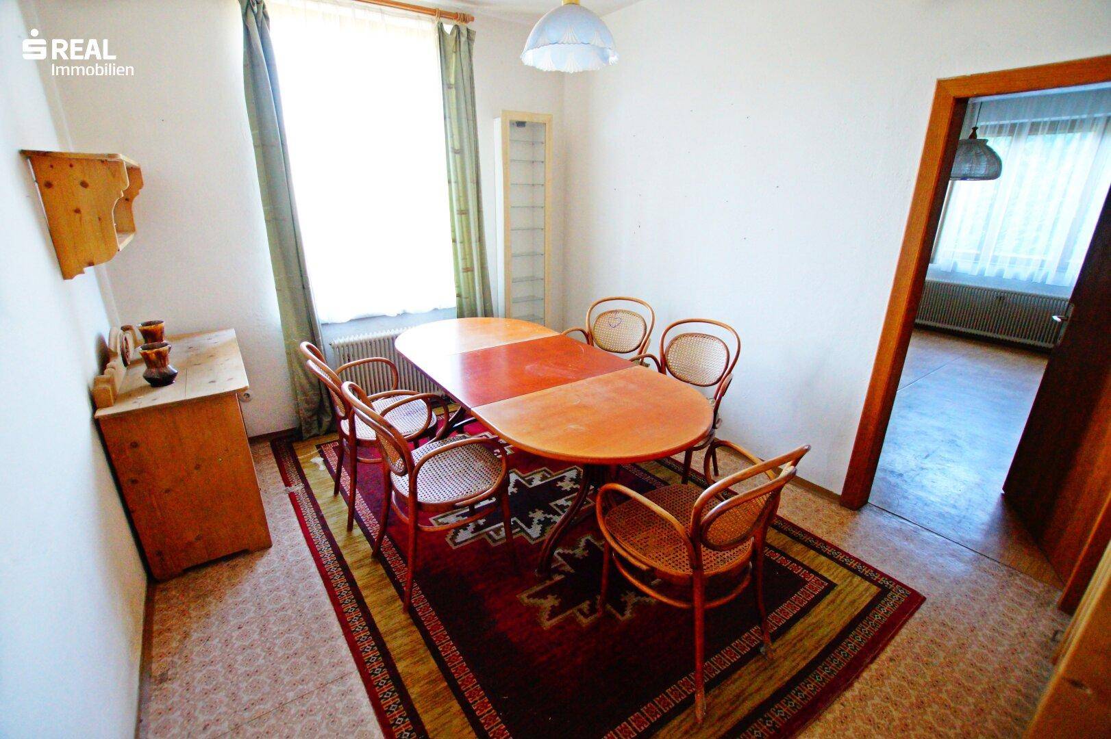 Gemütlicher Essbereich mit großem Holztisch, Stühlen und einem Teppich, ideal für Familienessen.