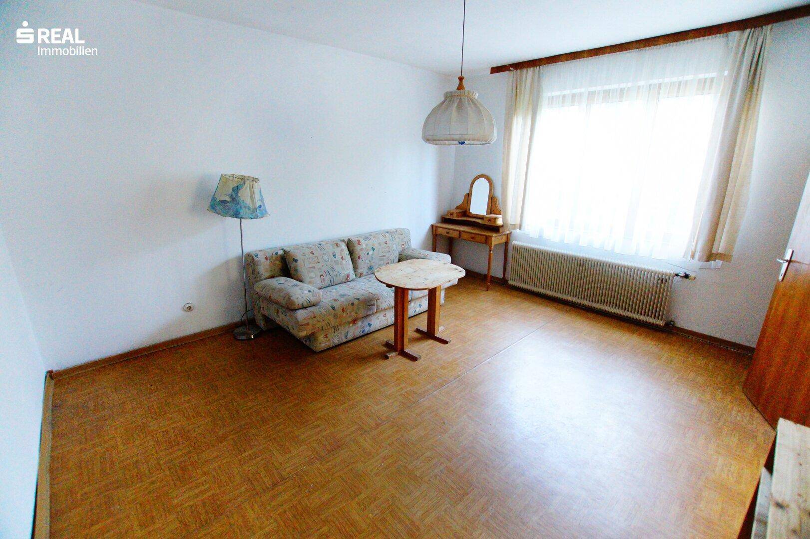 Heller Wohnraum mit Sofa, kleinem Tisch und Schminktisch, ausgestattet mit Parkettboden.