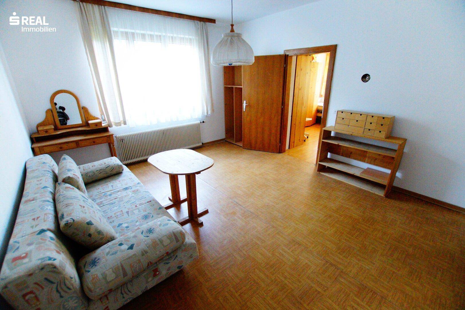 Wohnzimmer mit Sofa und Parkettboden, bietet Zugang zu einem angrenzenden Raum.