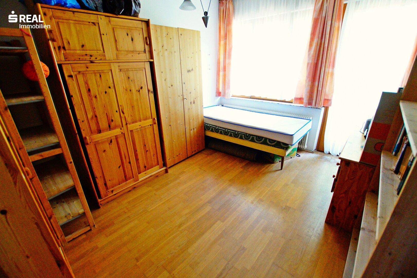 Schlafzimmer mit Einzelbett, großen Holzschränken und Parkettboden, bietet viel Stauraum.